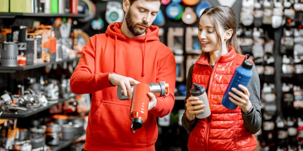 Young couple dressed in red sportswear choosing dishes for camping in the shop with travel equipment